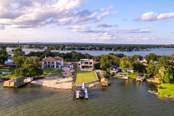Aerial view of a stunning luxury lakehouse on Lake LBJ, custom-built by Zbranek & Holt Custom Homes. This elegant waterfront property features a private boat dock, expansive green lawn, and sophisticated modern architecture, reflecting the builder’s commitment to craftsmanship and luxury. Nestled among other exclusive lakefront homes, this custom masterpiece showcases Zbranek & Holt’s dedication to creating beautiful, high-quality residences that perfectly blend with the scenic surroundings of Lake LBJ.