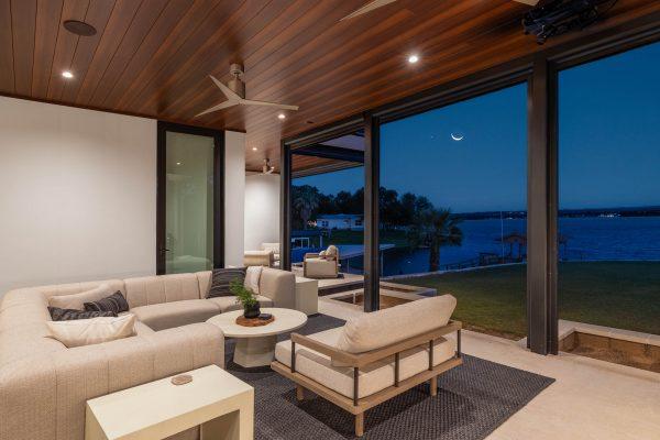 Modern luxury lakehouse covered patio lounge with comfortable seating, wood-paneled ceiling, and open view of Lake LBJ at twilight, designed by Zbranek & Holt Custom Homes.